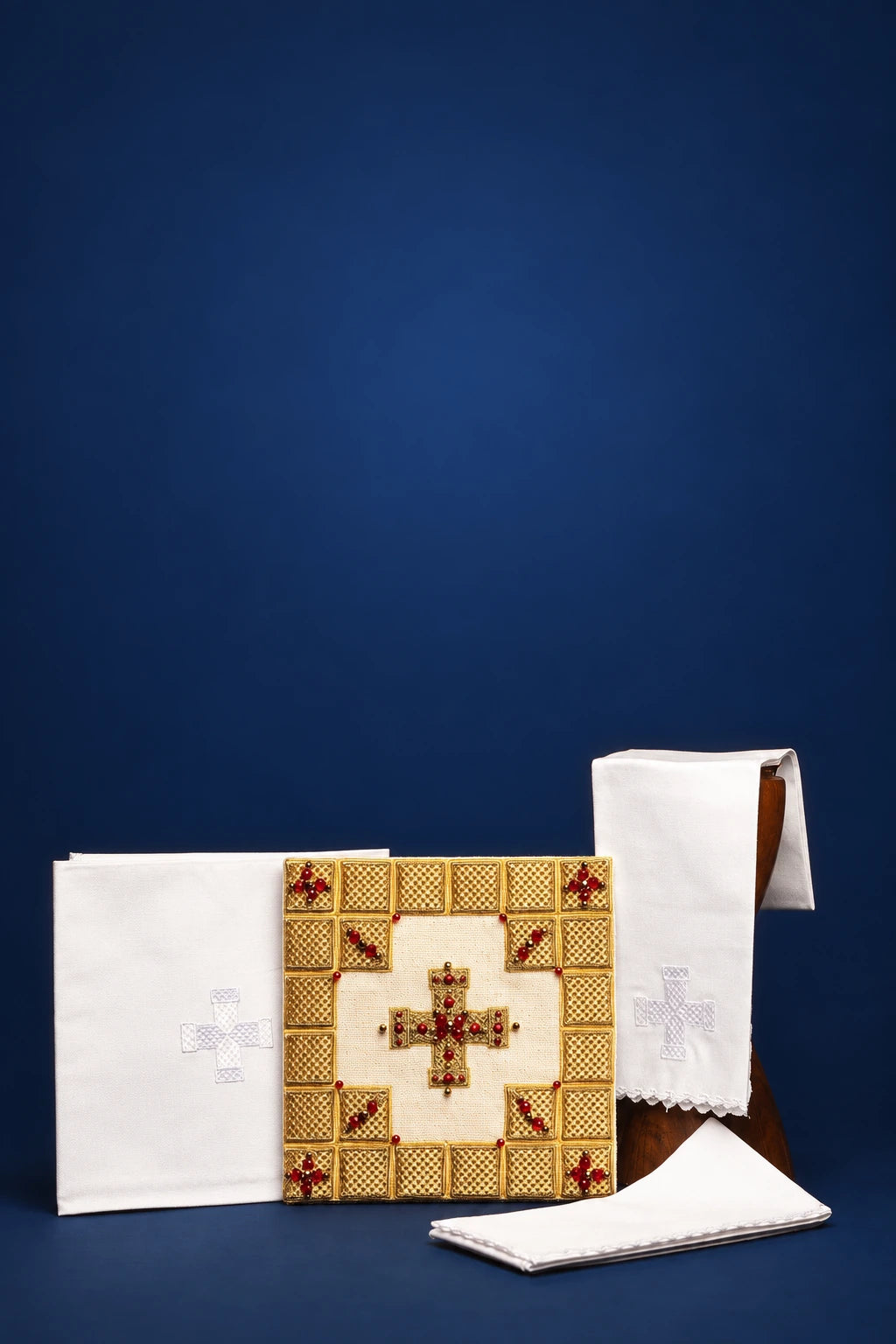 Altar linen set with embroidered cross, folded white linens, and a square altar cloth with gold and red mosaic cross design