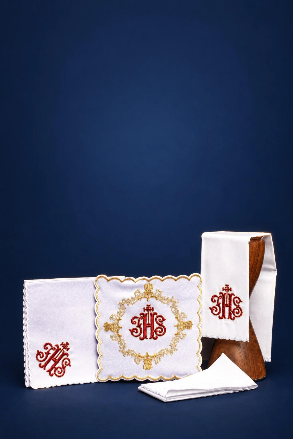 Altar linen set with red embroidery, showing folded purificator, corporal, and pall with gold monogram motif