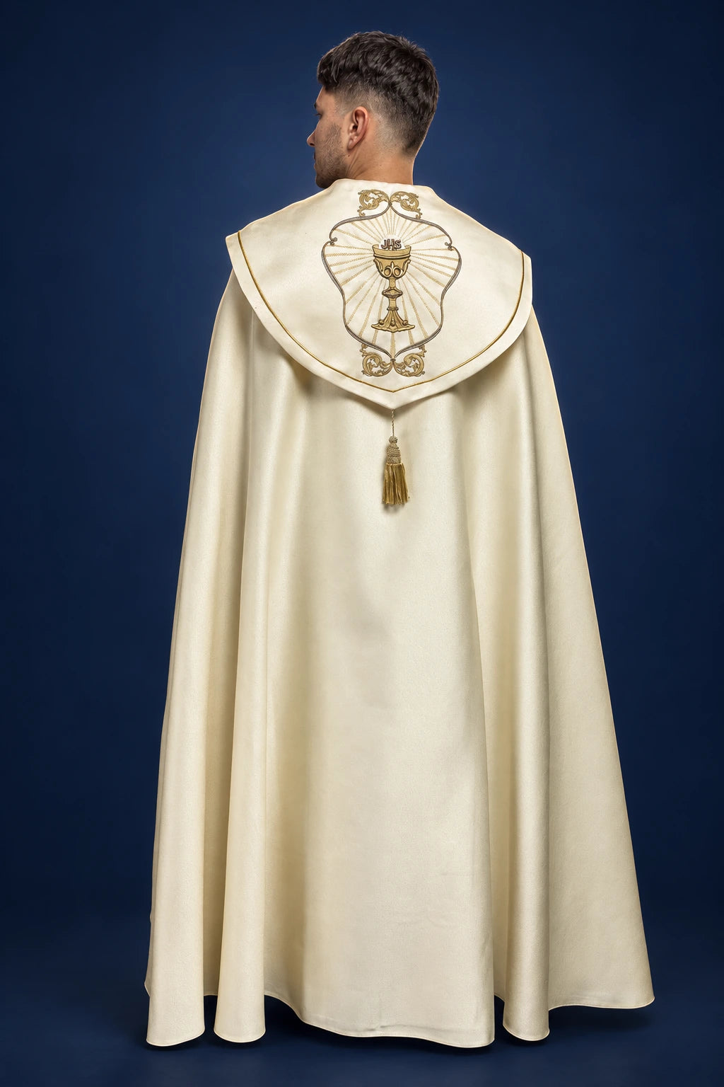 Back view of an ecru cope with a central hood medallion and a dangling gold tassel clasp