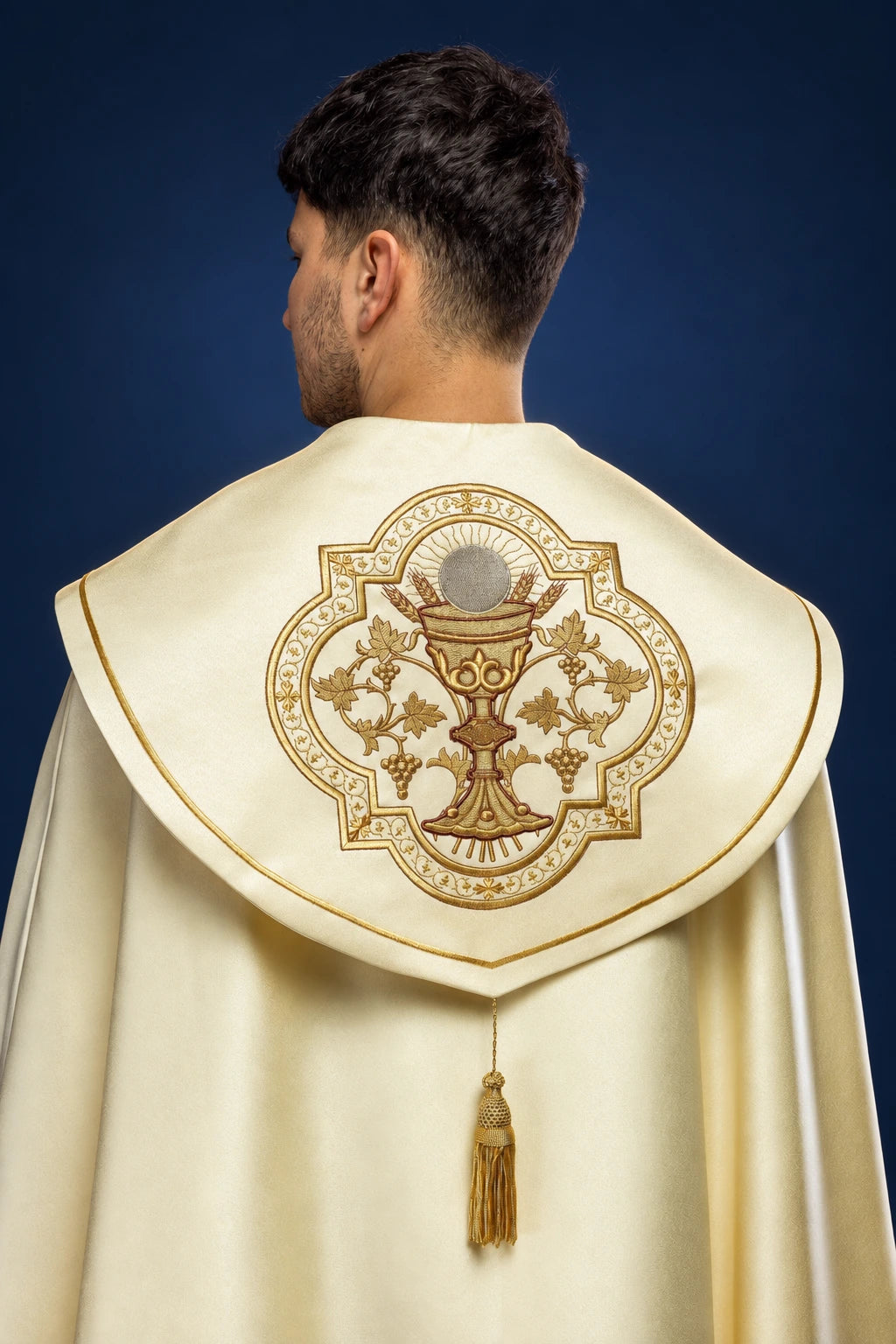 Back view of an ecru cope with gold trim and a large embroidered chalice motif on the capelet back.