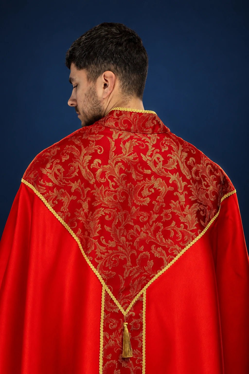 Back view of a red cope with gold trim and ornate jacquard panel, fastened with a tassel clasp
