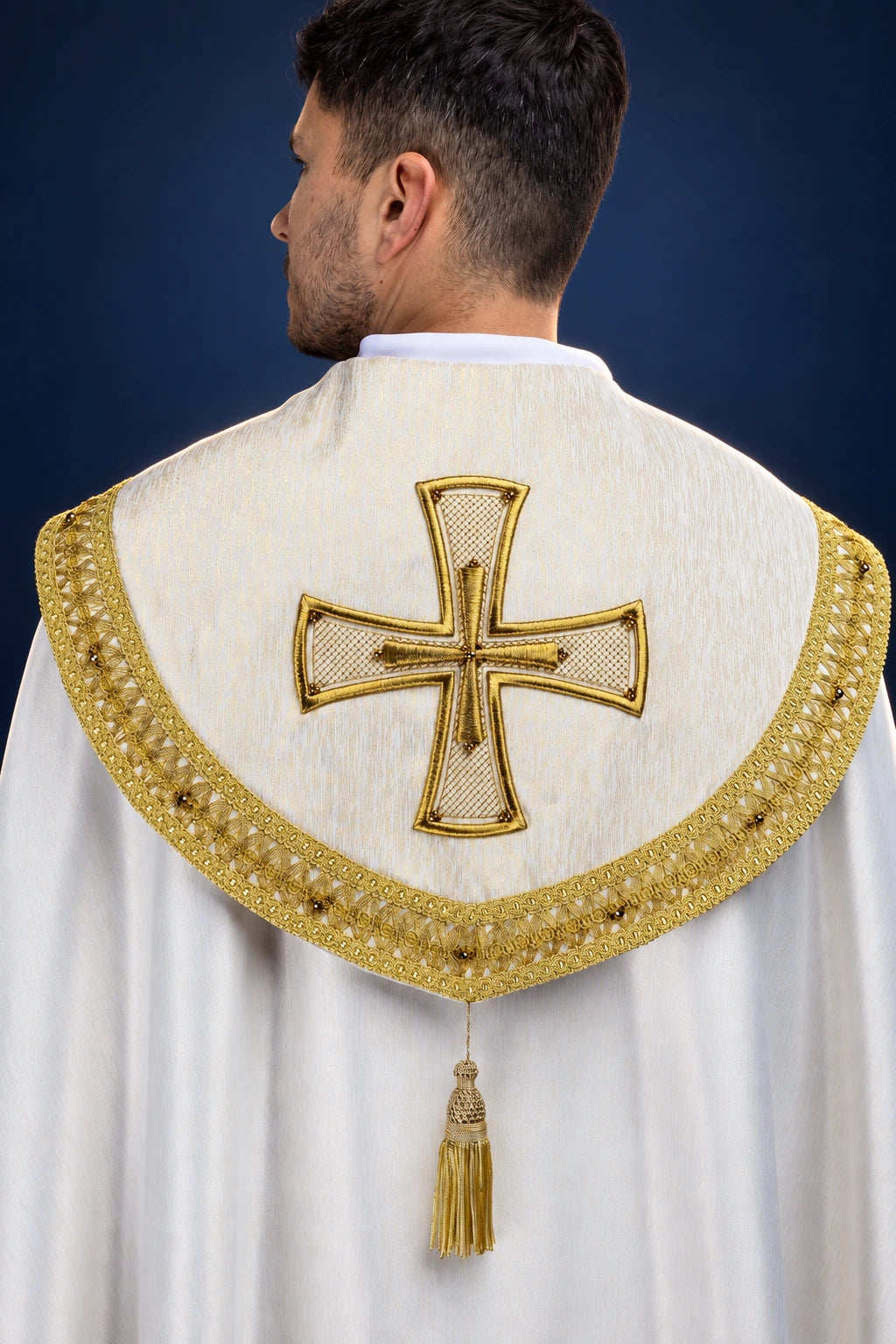 Back view of a white cope with gold-trimmed circular capelet, jeweled cross, and tassel clasp