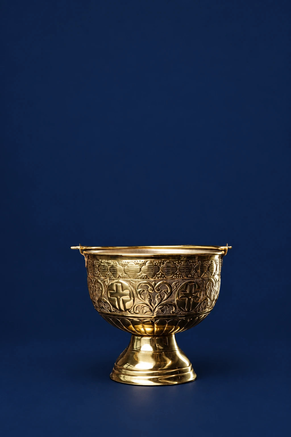 Brass holy water bucket with pedestal base and embossed cross and floral scrollwork, front view