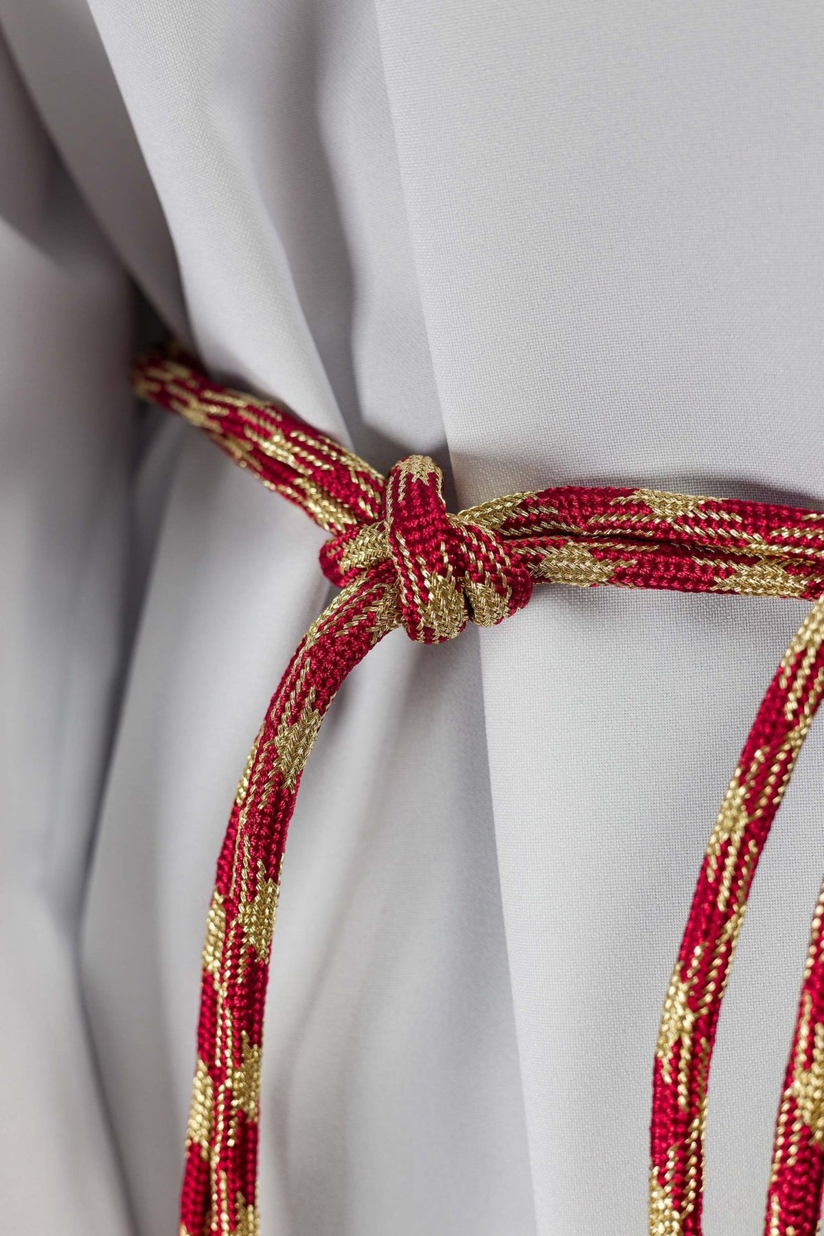 Red and gold cincture close-up showing its braided knot and patterned cord