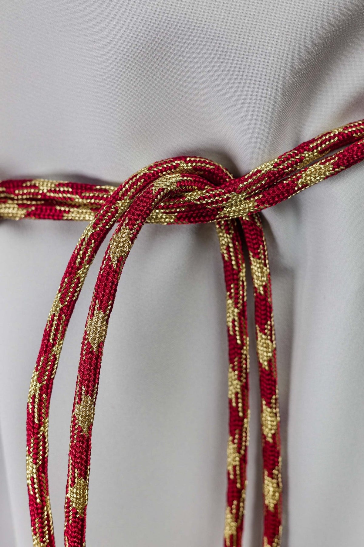 Red and gold cincture close-up showing braided cord detail and knot