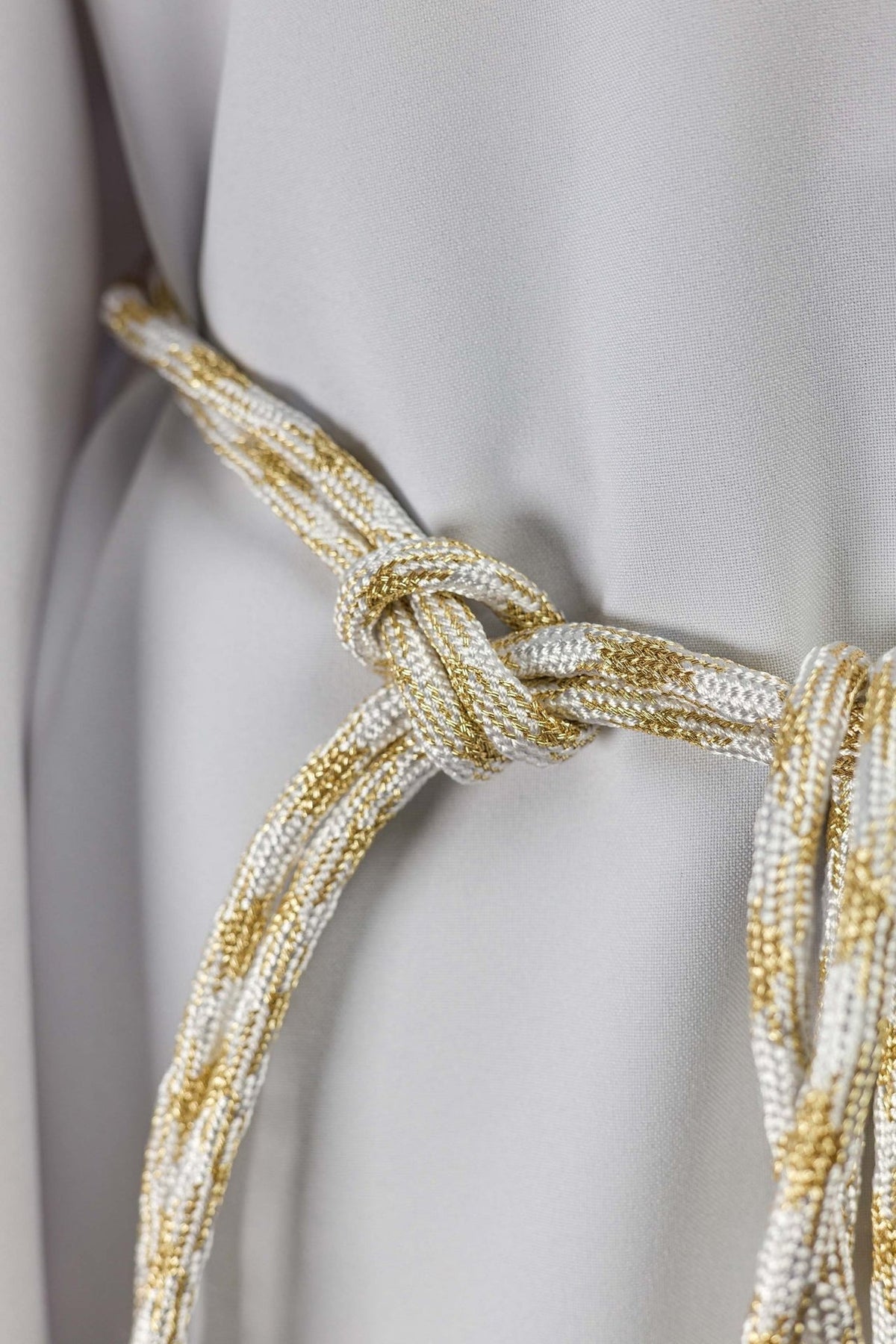 White and gold cincture close-up showing braided cord and tied knot