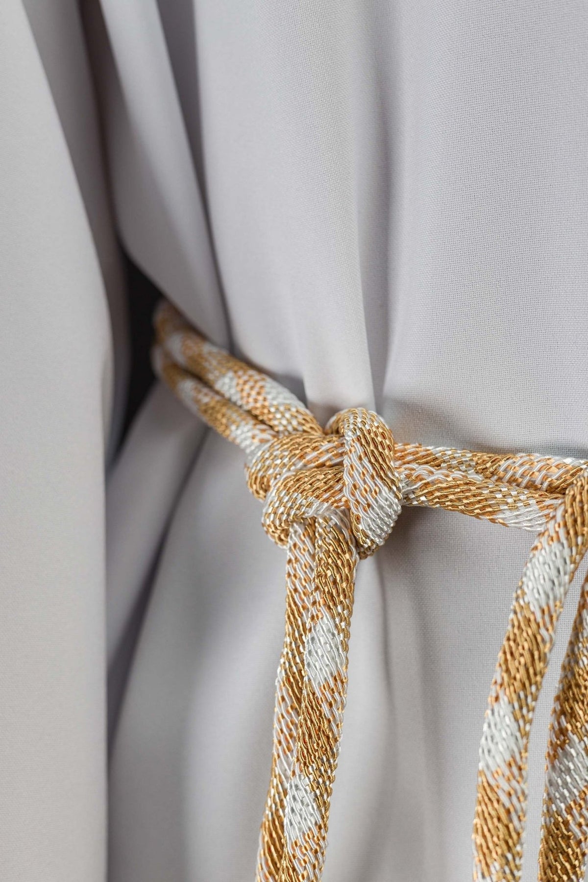 White and gold cincture close-up showing its braided knot