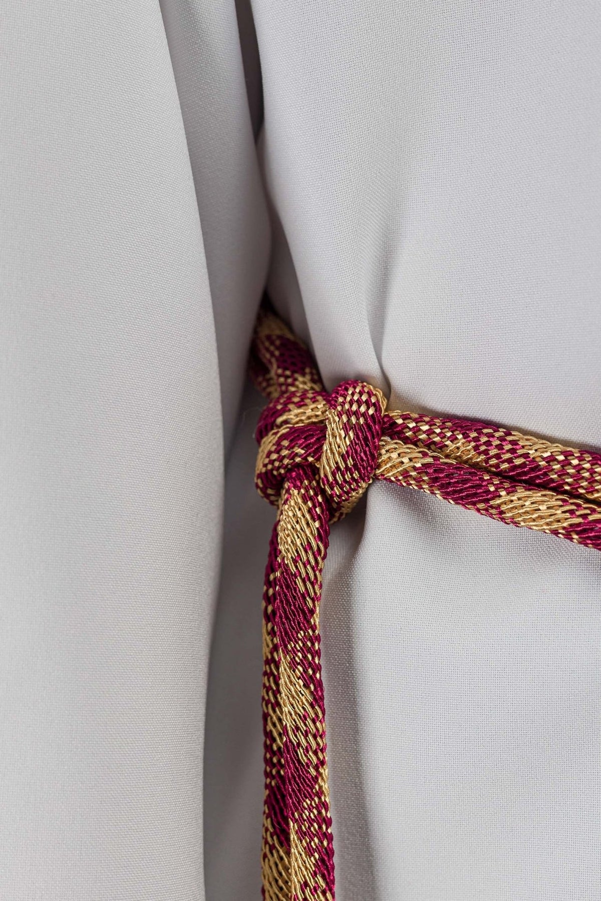 Red-and-gold cincture close-up showing the tied knot and woven pattern