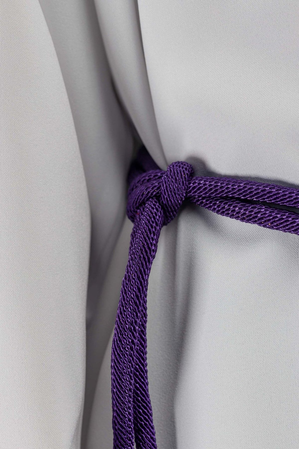 Purple liturgical cincture close-up showing braided cord tied around the alb
