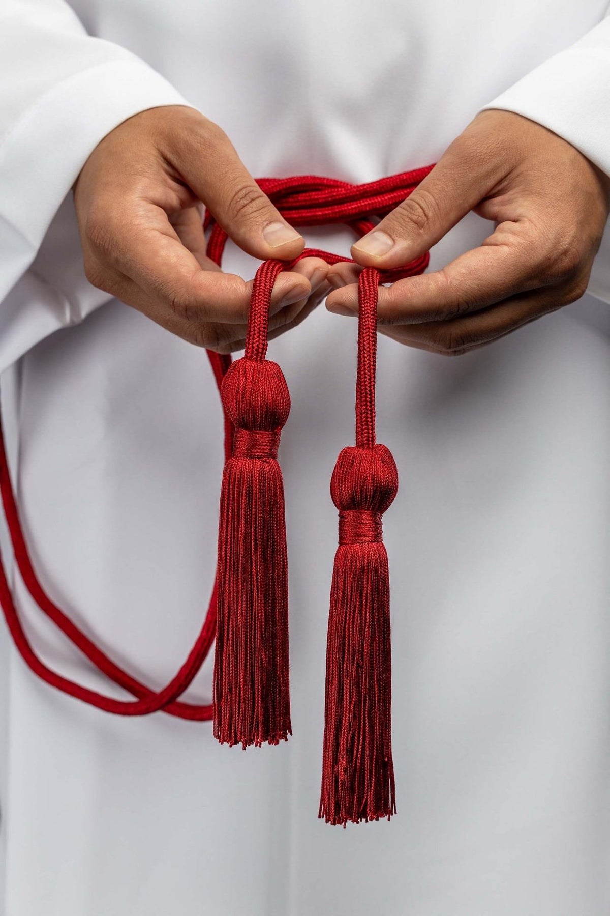 Red liturgical cincture held to show its two long decorative tassels and braided cord