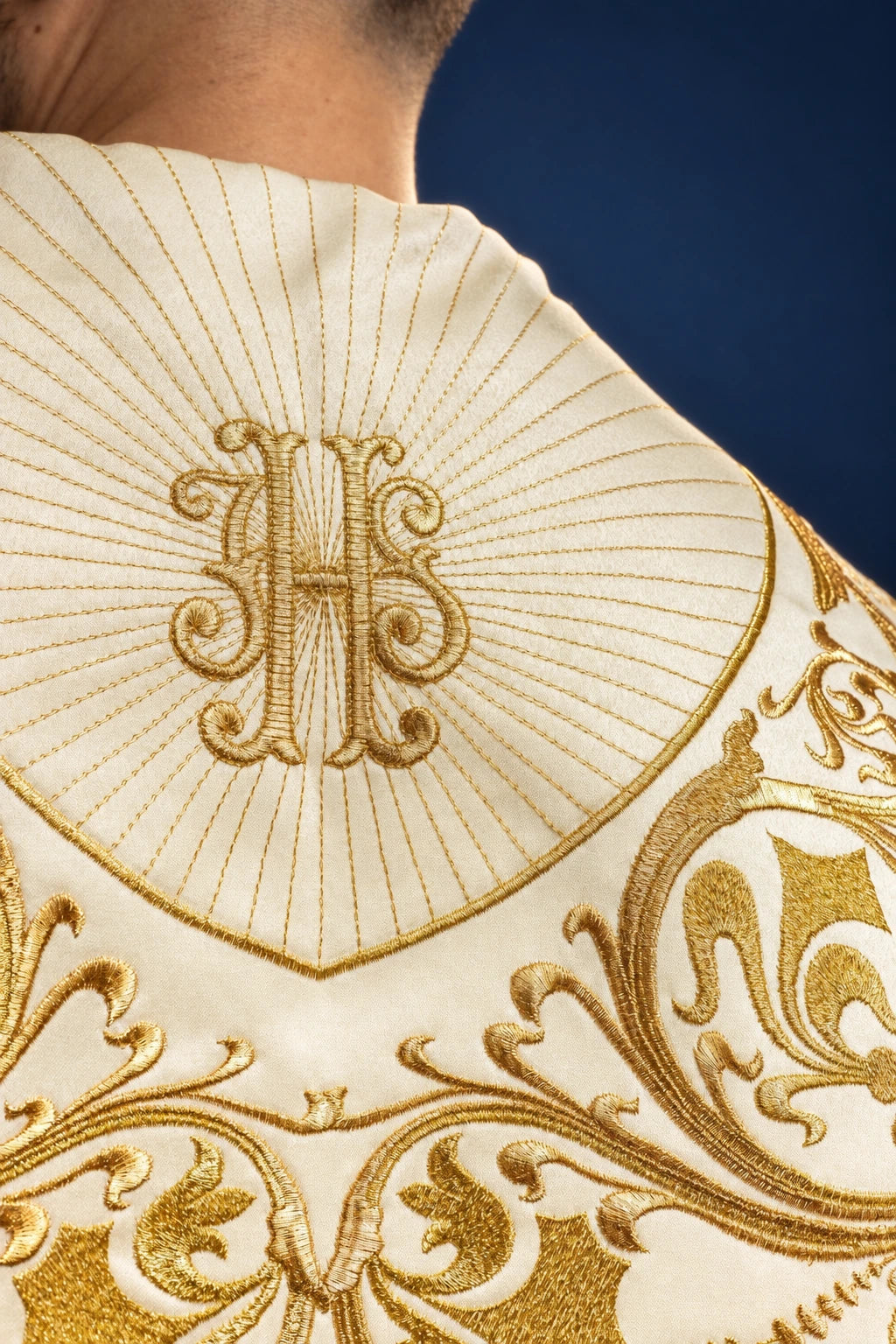 Close-up of the cope’s hood with gold IHS monogram and radiating stitched rays above ornate scrollwork