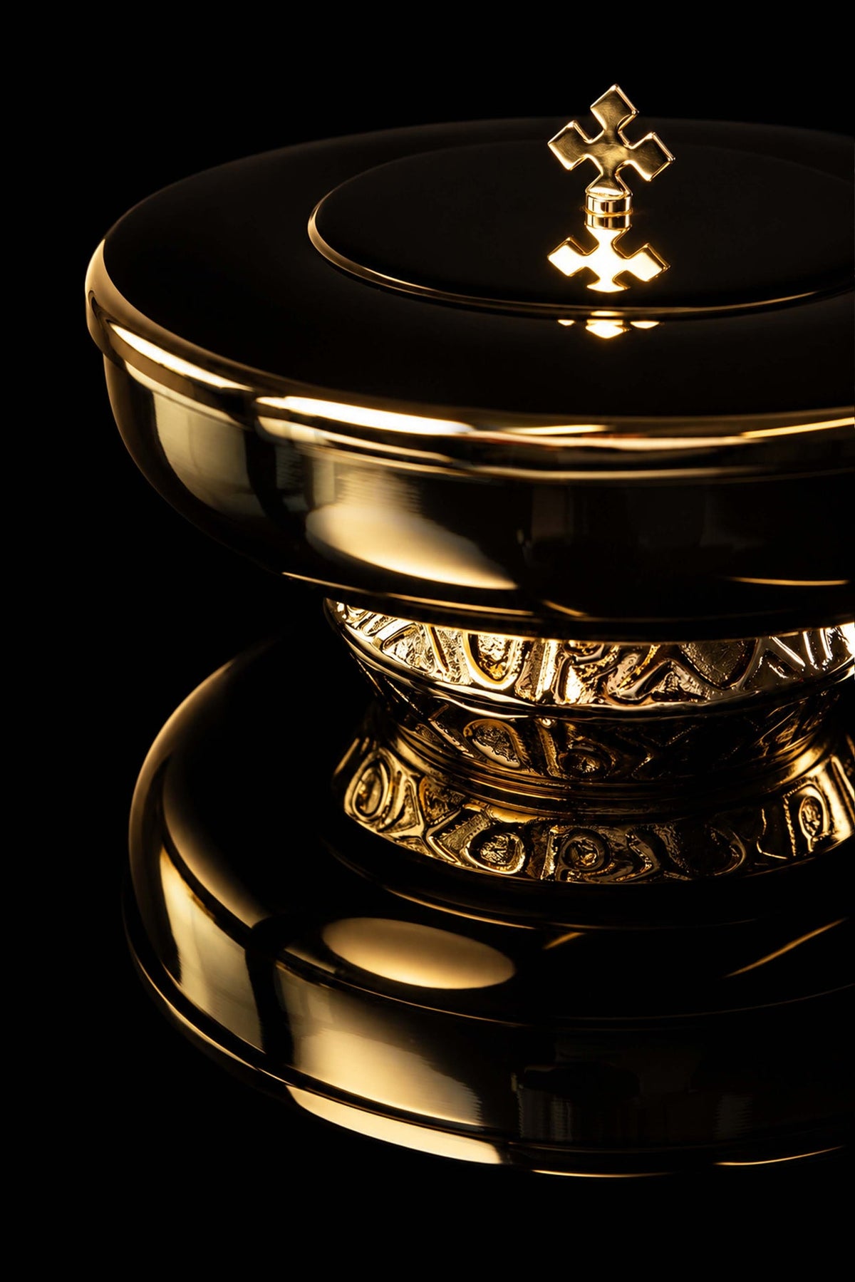 Gold-plated brass ciborium close-up showing cross finial, lid rim, and embossed base