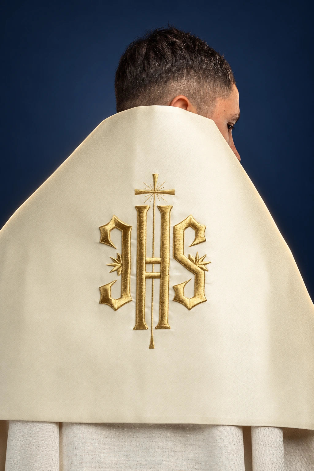 Ecru humeral veil draped over the shoulders, three-quarter view, with gold embroidered IHS symbol on the back panel