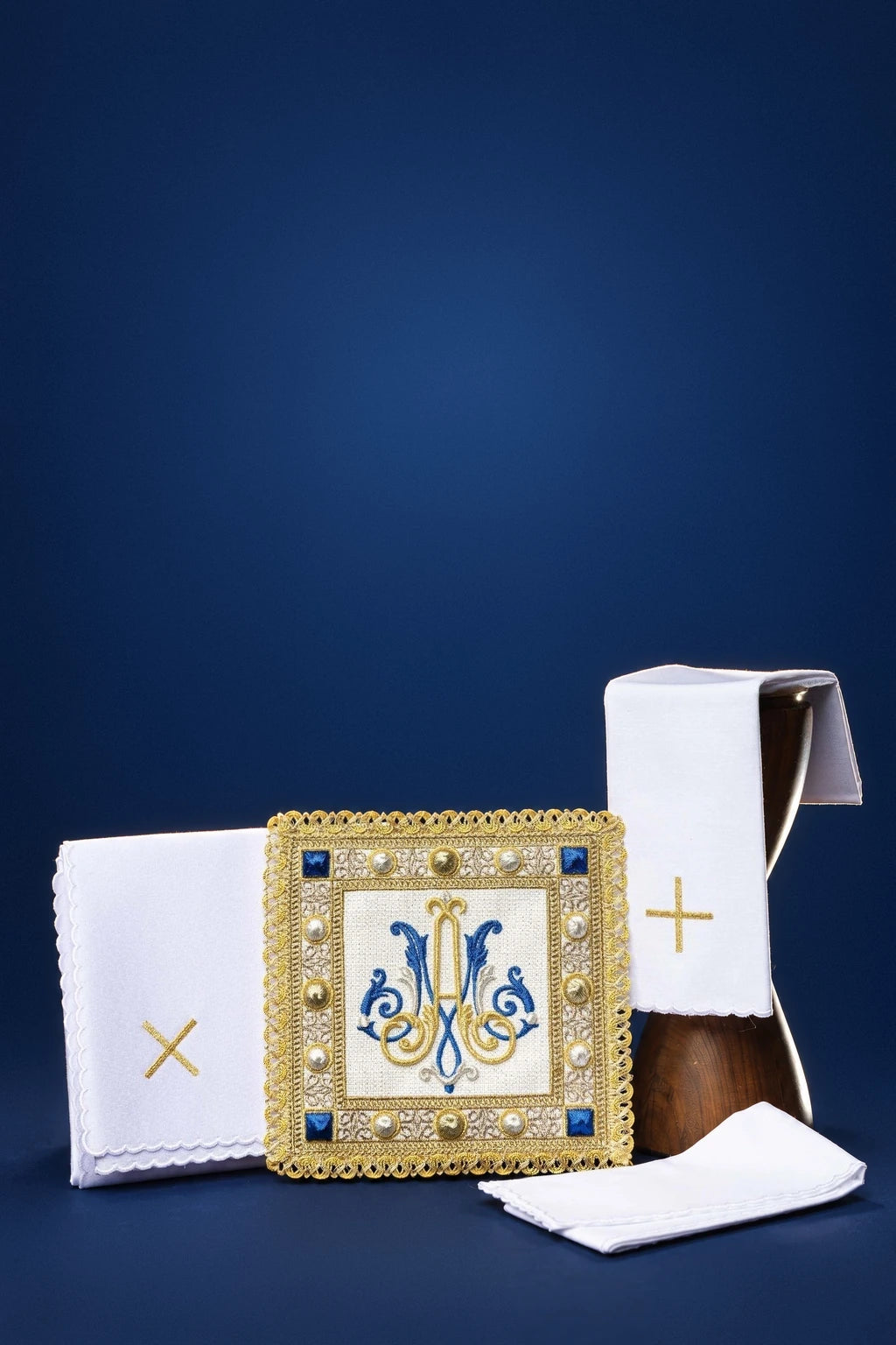 Embroidered altar linen set with Marian monogram and gold cross accents on folded linens