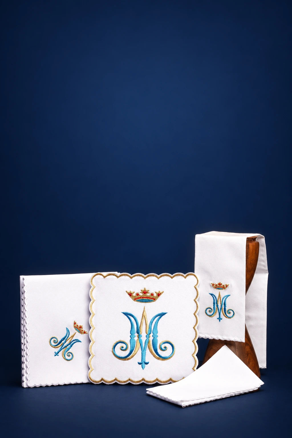 Embroidered Marian altar linen set with folded white cloths, central monogram square, and matching cross-stitched motifs