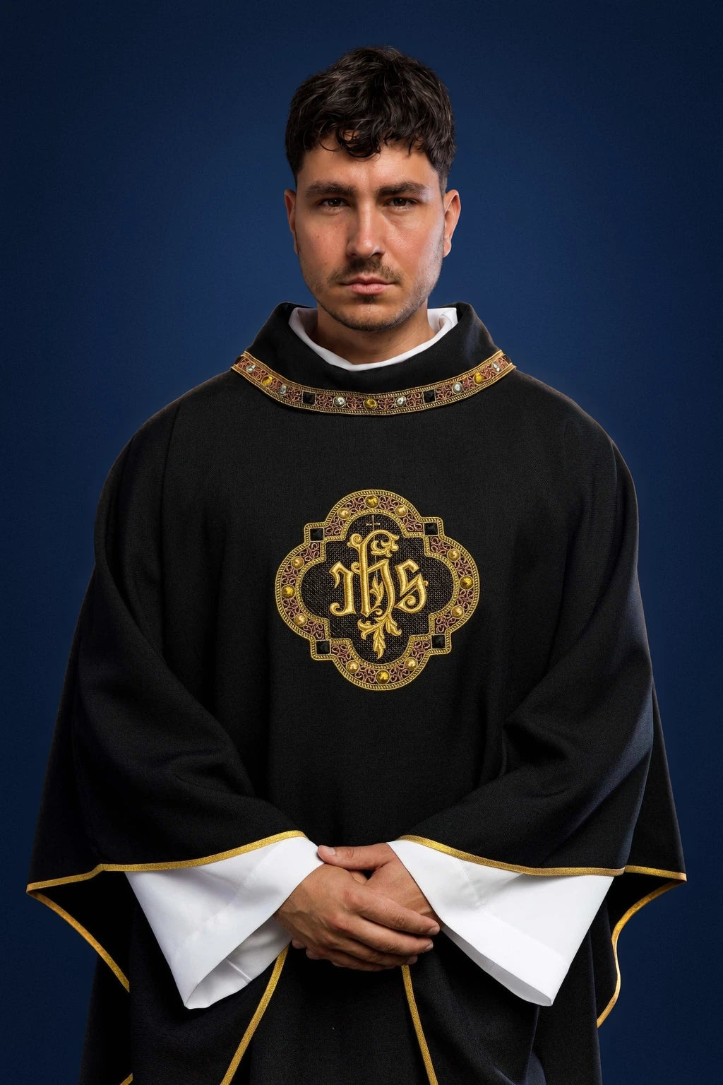 Front view of a black chasuble with gold trim and IHS embroidery on the chest and collar.