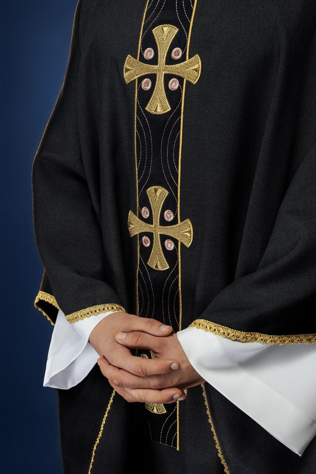 Front view of a black chasuble with vertical gold cross embroidery and gold-trimmed sleeves and hem