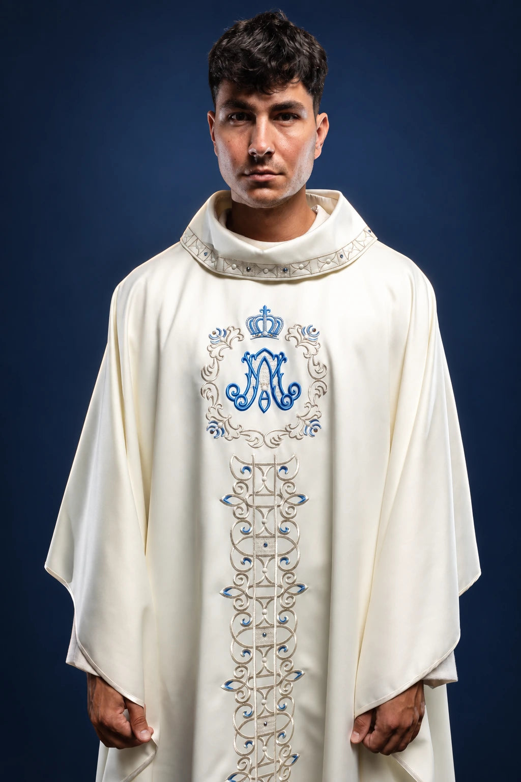 Front view of a cream Marian chasuble with embroidered blue Marian monogram and vertical orphrey band