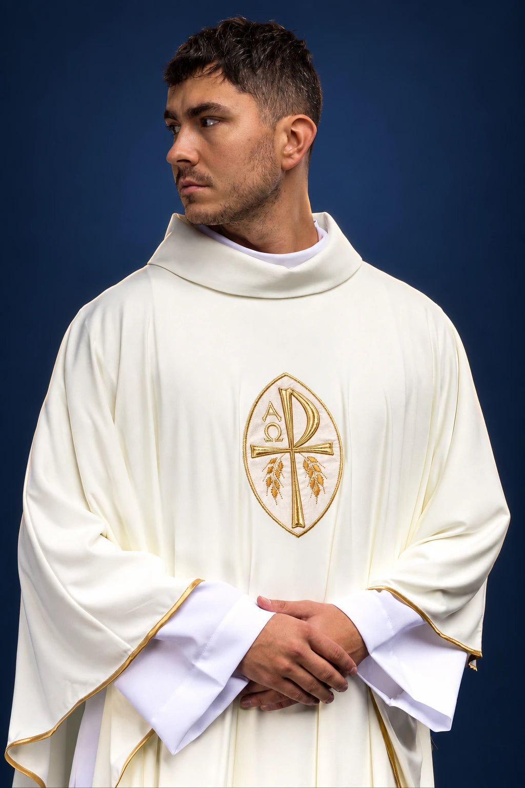 Front view of an ecru chasuble with gold-embroidered Christogram and trim, worn over white sleeves