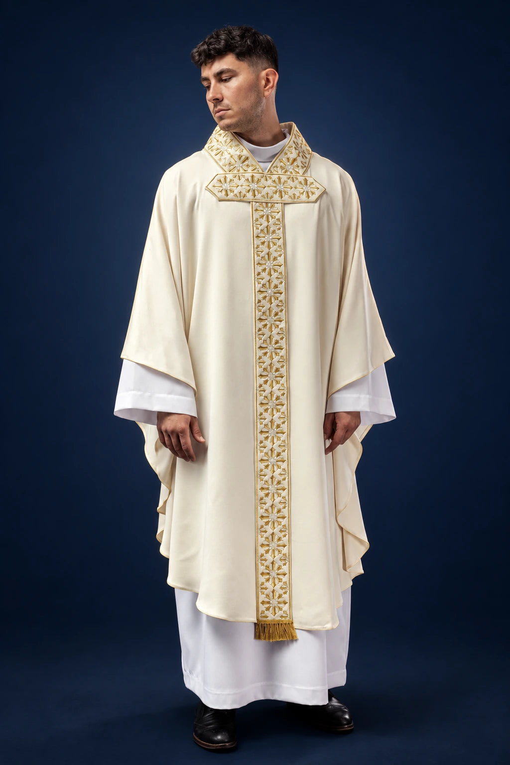 Front view of an ecru chasuble with gold embroidered cross and vertical stole panel, with fringe at hem