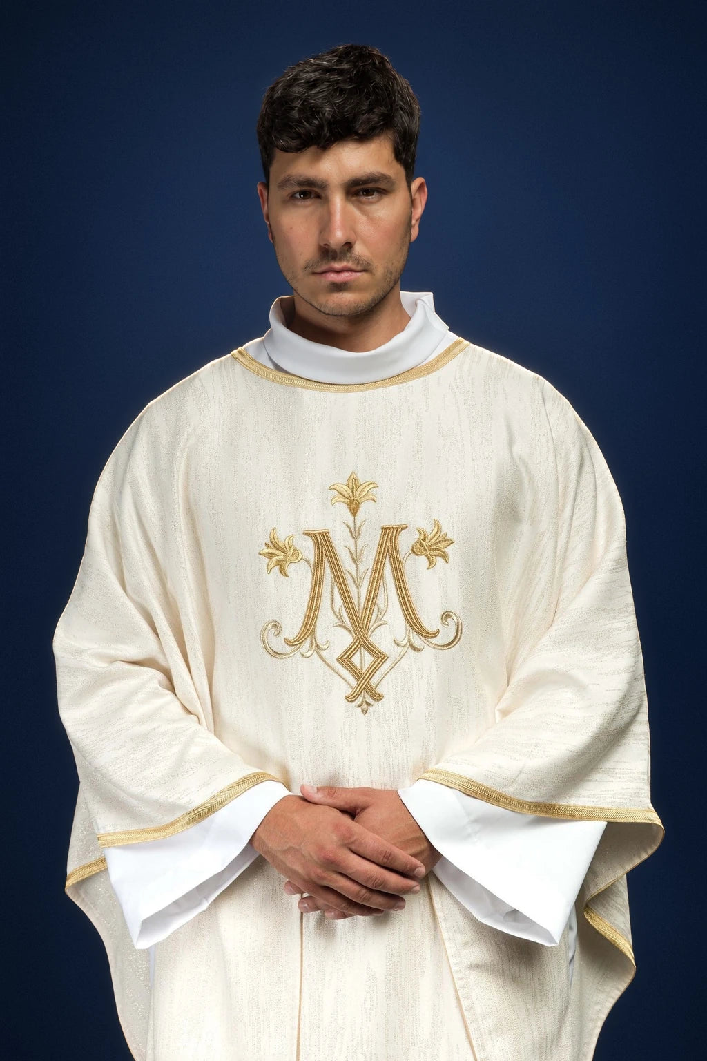 Front view of an ecru chasuble with gold trim and a centered embroidered Marian monogram