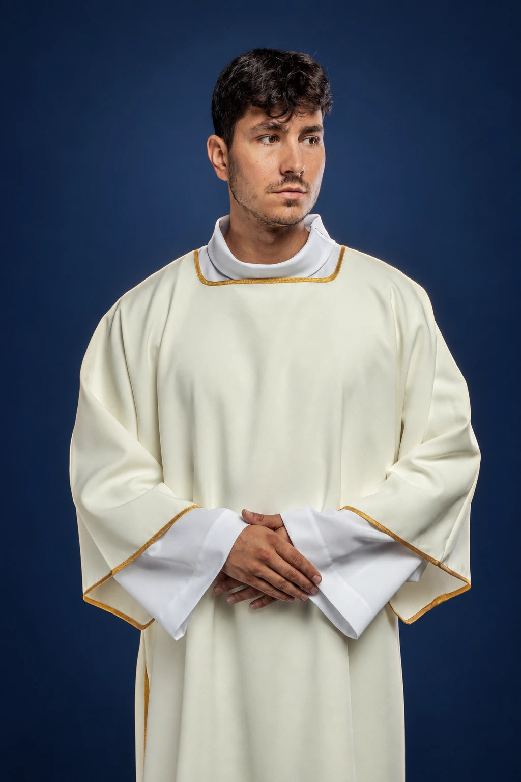 Front view of an ecru dalmatic with gold trim and wide sleeves, worn over a white alb