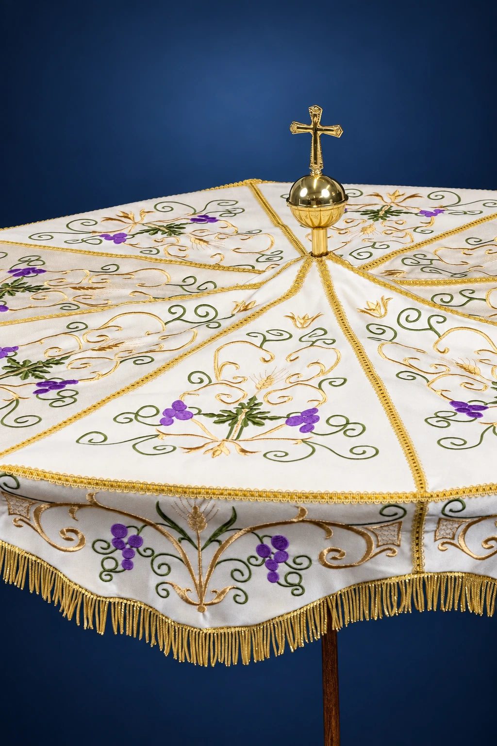 Front view of ecru processional umbrella with gold trim and colorful floral embroidery, topped with a gold cross finial