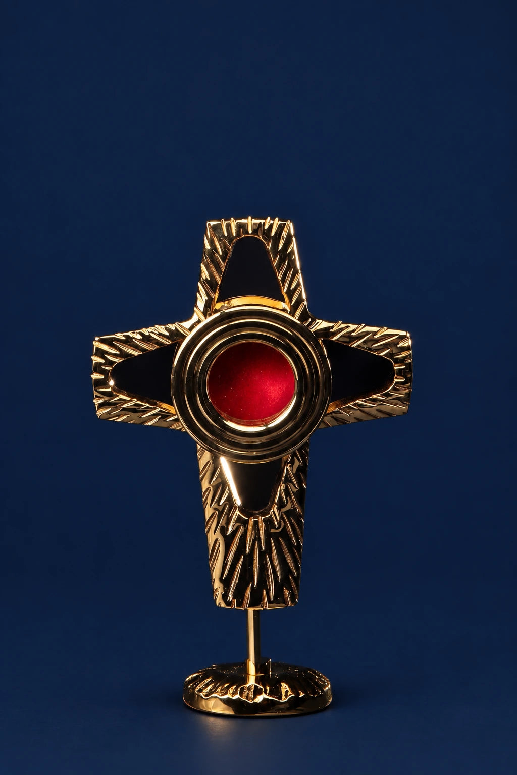 Front view of a gilded brass cross-shaped reliquary on a stand, with a red center medallion