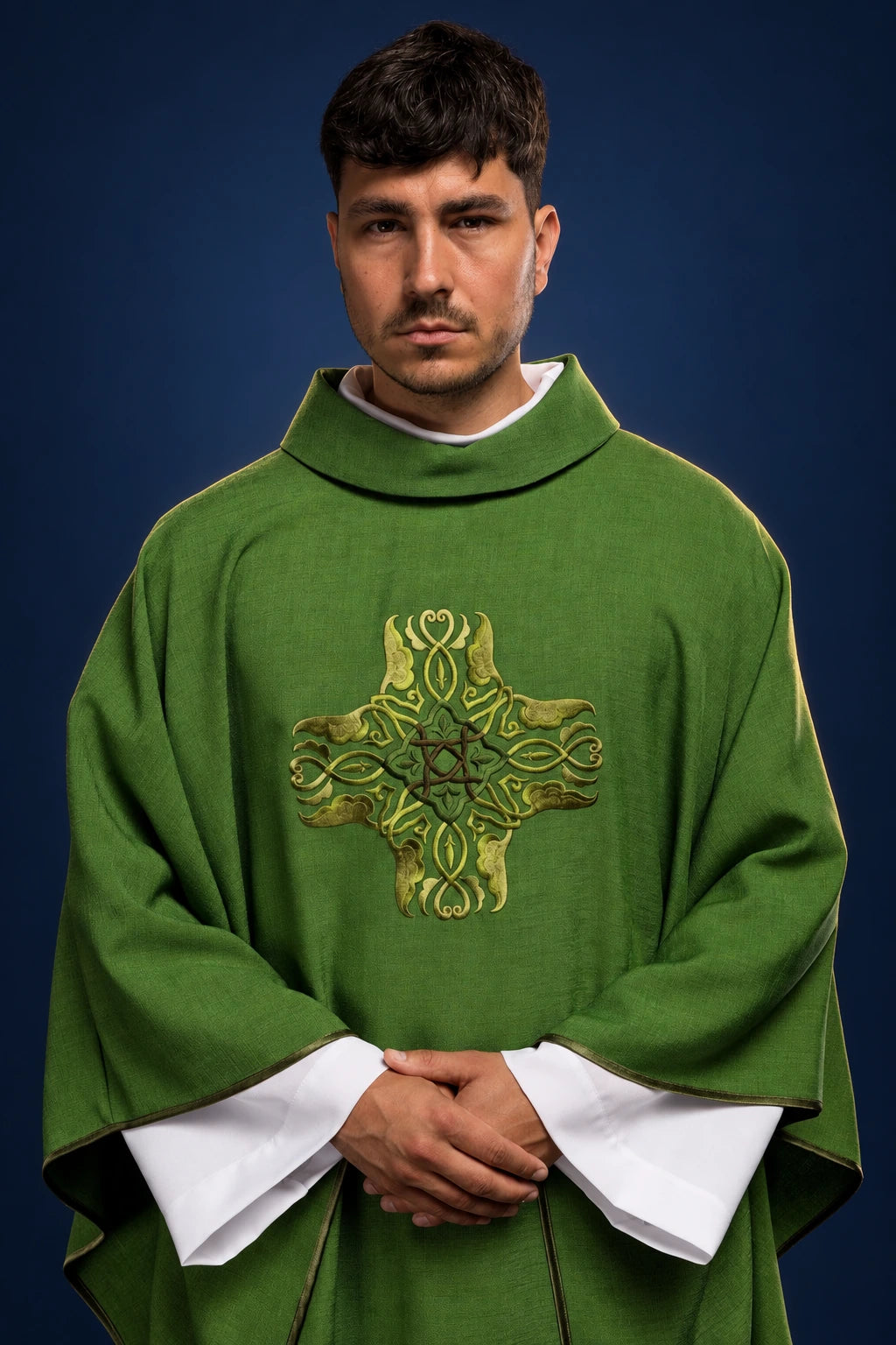 Front view of a green chasuble with ornate cross embroidery and wide sleeves over white vestments