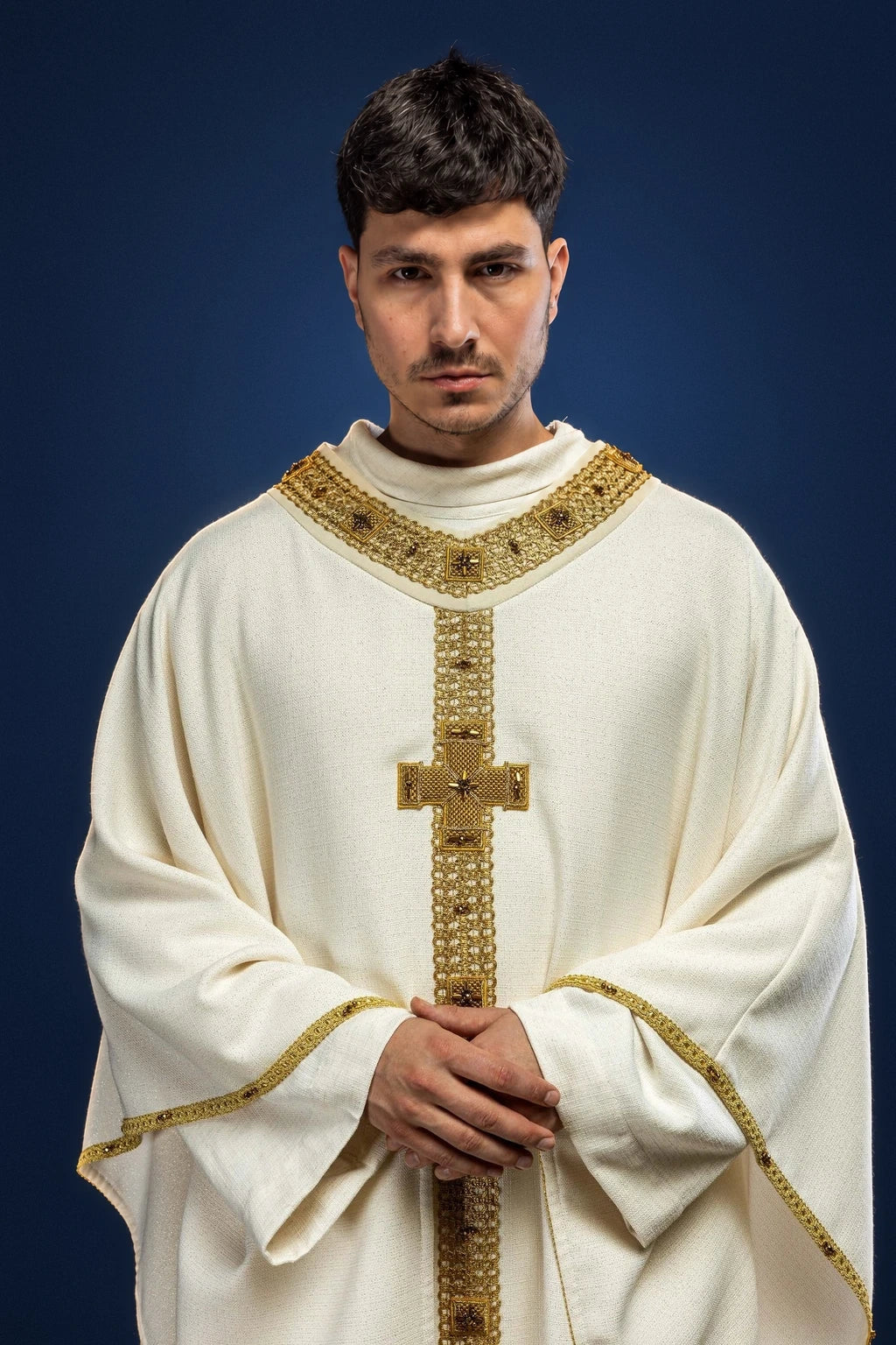 Front view of an ivory chasuble with gold trim, stone-like vertical panel, and gold cross motif at the chest