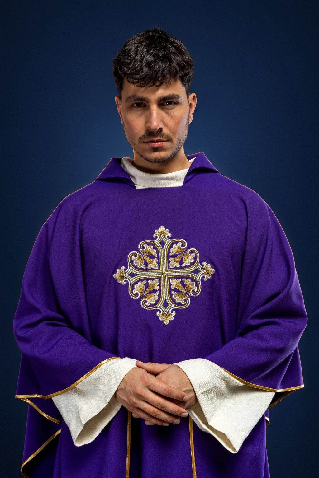 Front view of a purple chasuble with a gold embroidered cross and wide square collar over white sleeves.