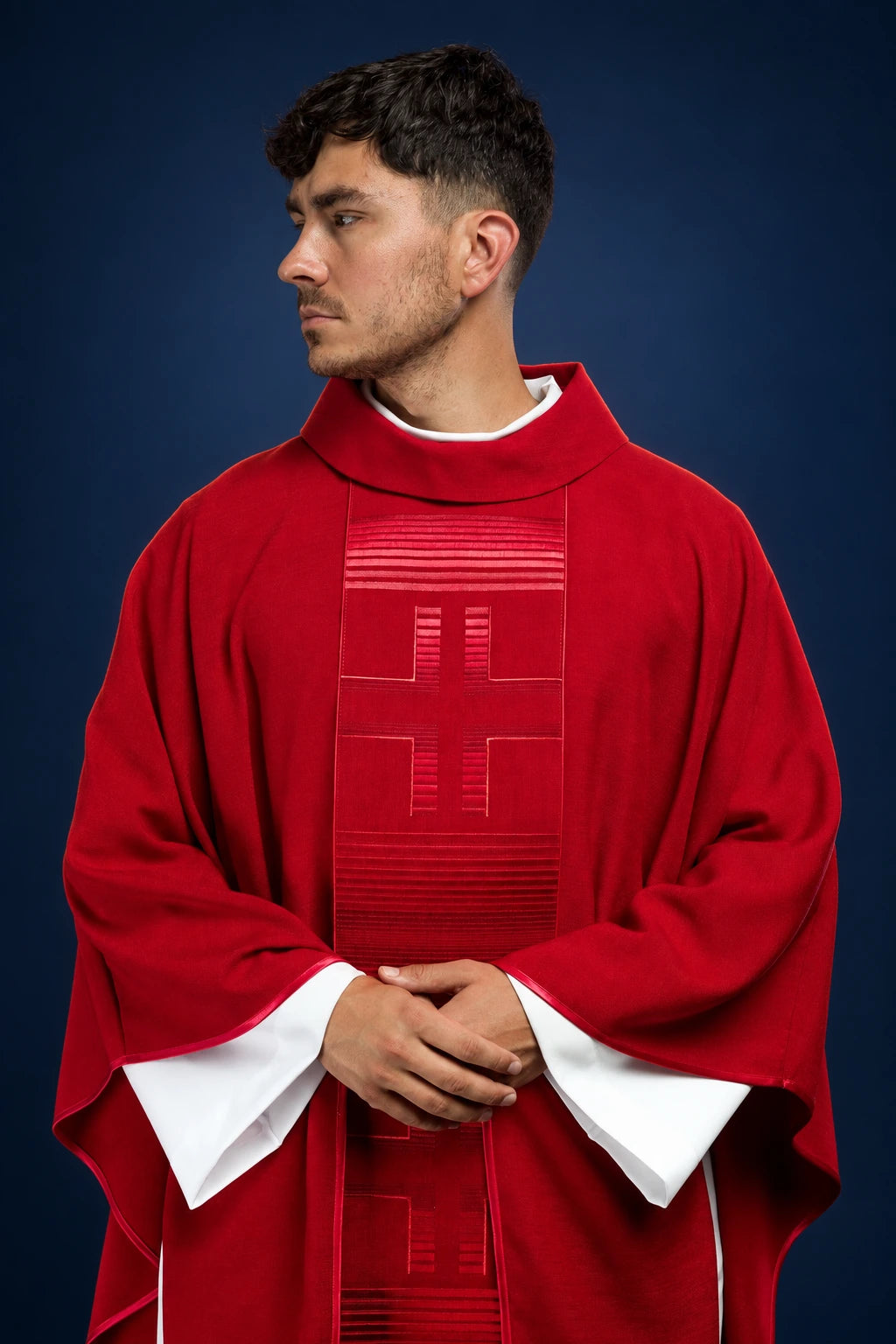 Front view of a red chasuble with embroidered cross panel and white sleeves showing at the cuffs