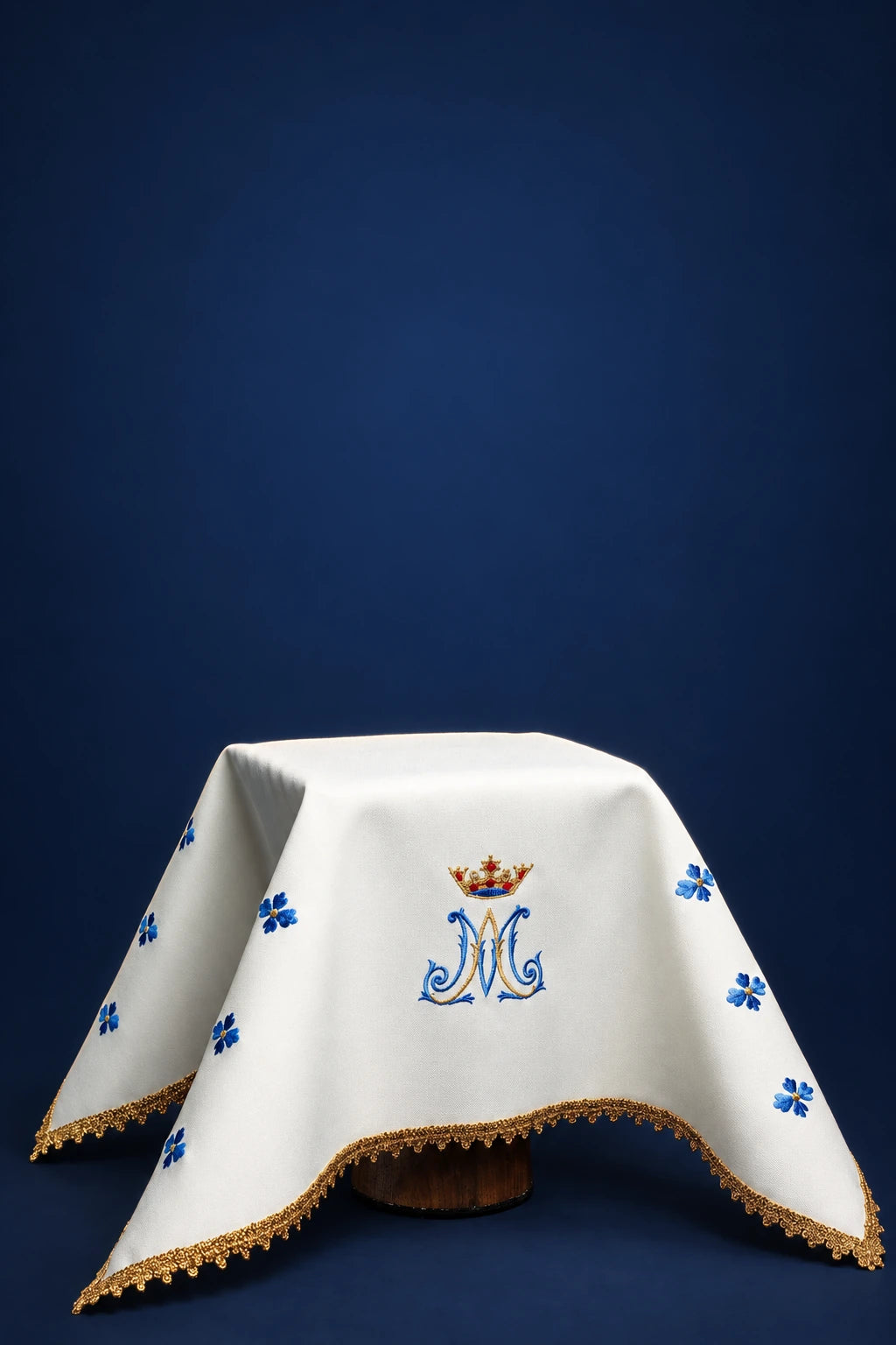 Front view of a white chalice veil with blue Marian monogram and floral embroidery, gold lace trim