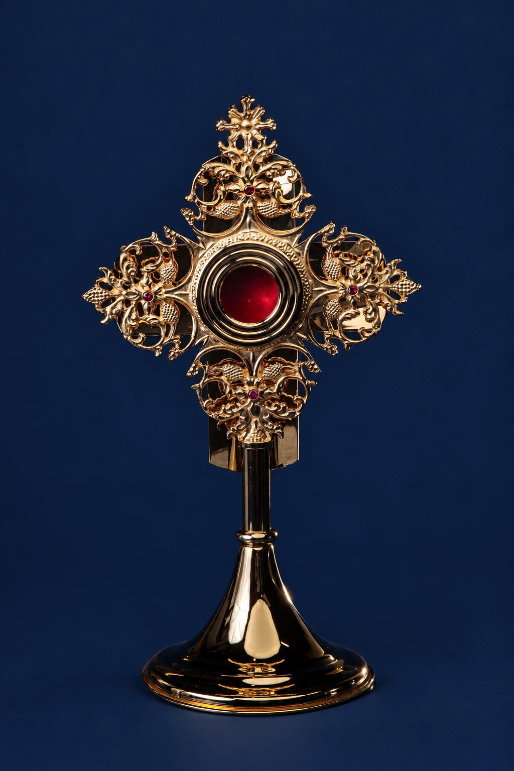 Gilded brass reliquary with ornate cross and red center, shown front view on a pedestal base