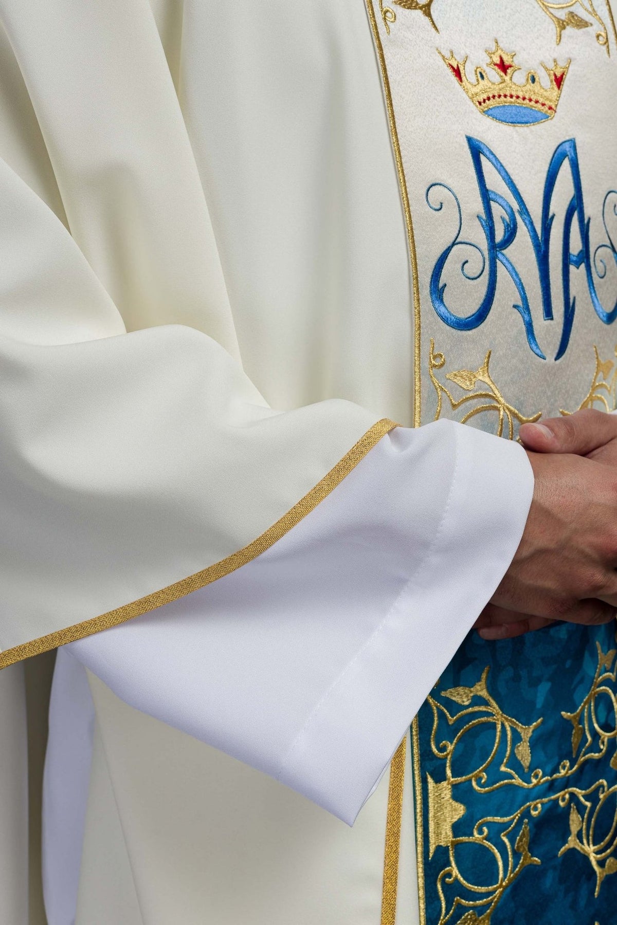 Close-up of ecru chasuble sleeve with gold trim and blue-and-gold embroidered orphrey