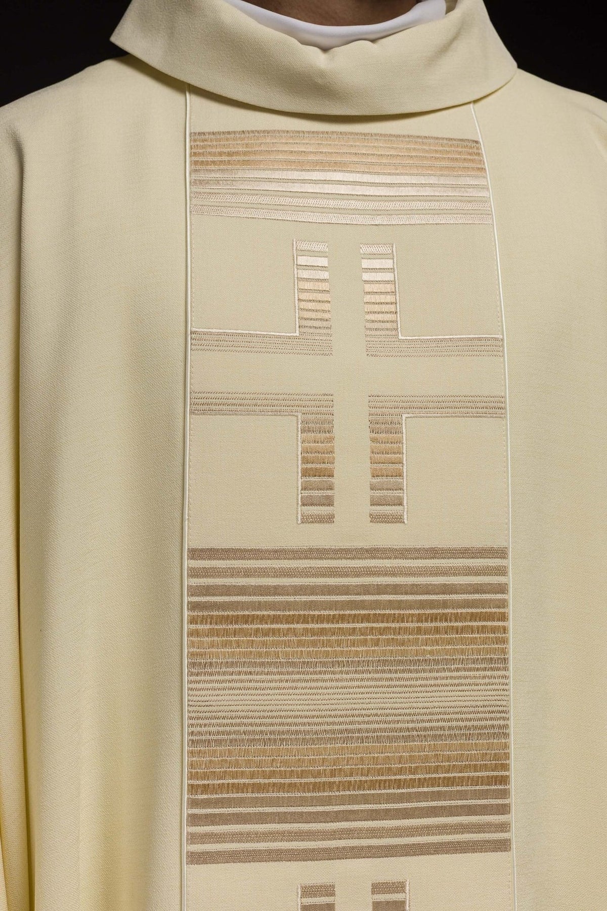 Ecru chasuble front close-up showing cross embroidery and horizontal striped trim