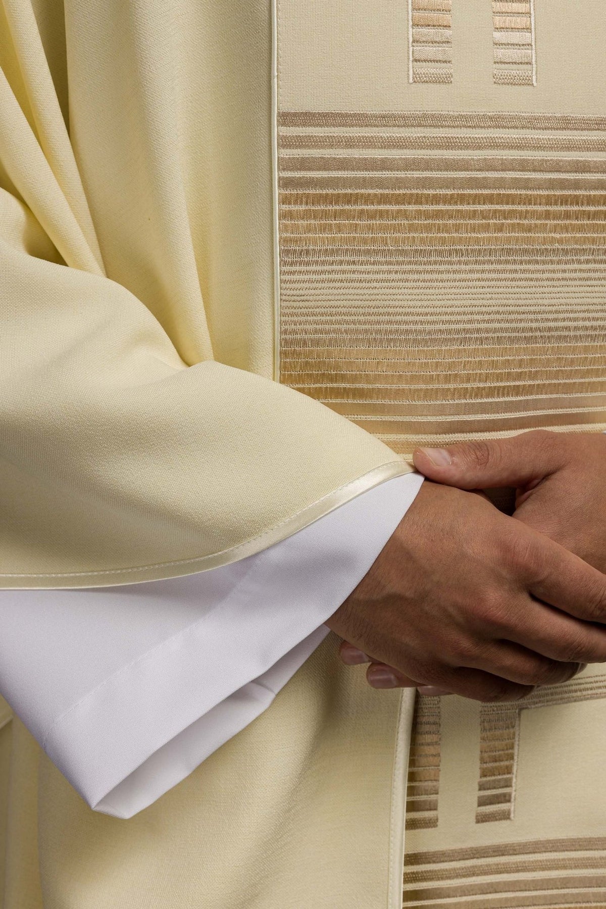 Ecru chasuble close-up showing striped embroidery, sleeve trim and fabric texture