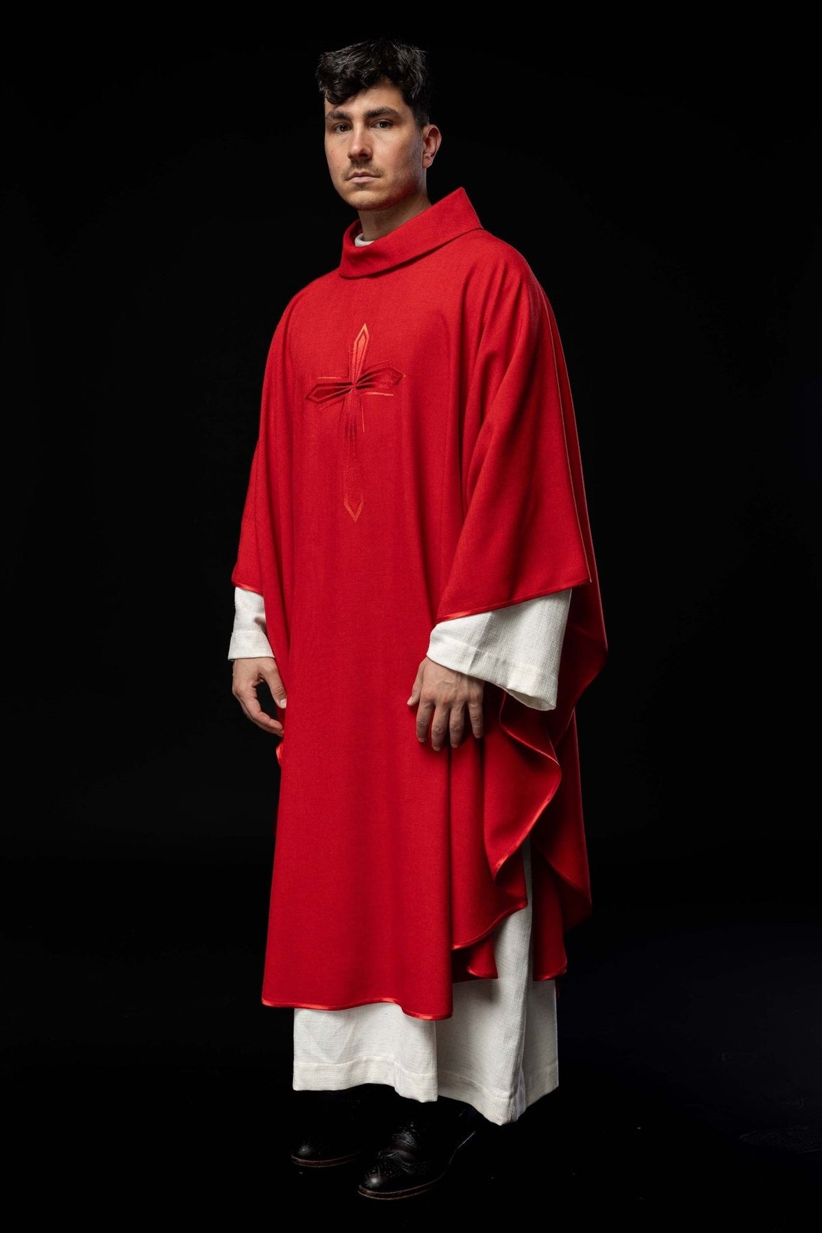 Red chasuble worn full length from the front, showing the embroidered cross and trim