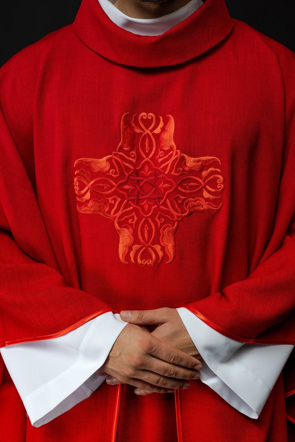 Red chasuble close-up showing ornate cross embroidery and satin trim