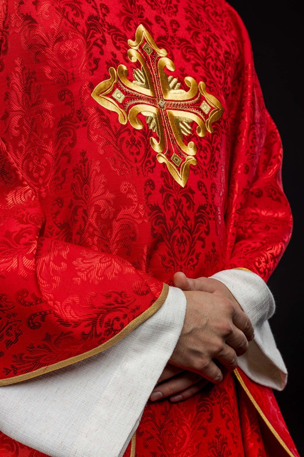 Red chasuble side close-up showing gold cross embroidery, patterned fabric and gold trim