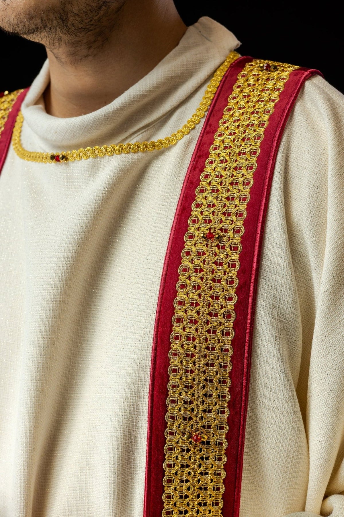 Dalmatic close-up showing red orphrey with gold embroidery and natural stones