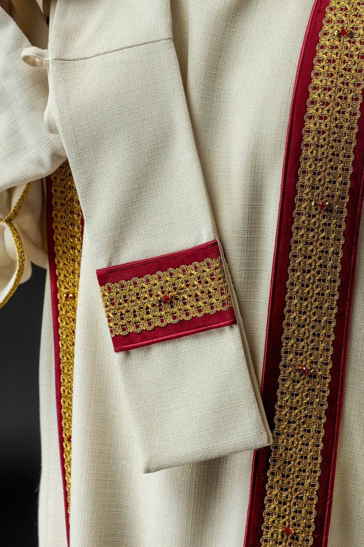 Dalmatic detail showing red cuff panel with gold embroidery and natural stones