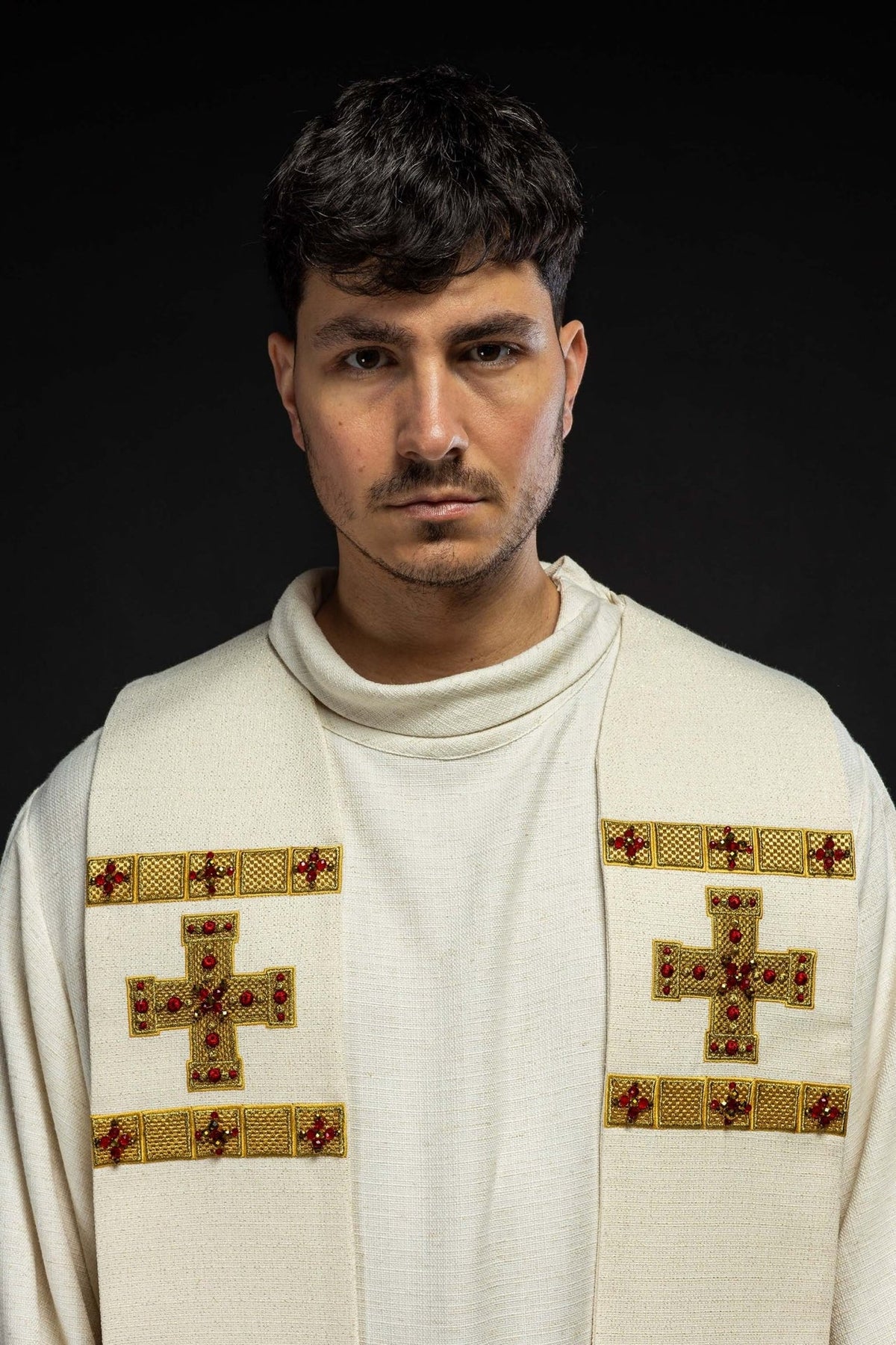 Stole close-up showing white fabric, gold embroidery, red stones and cross motifs