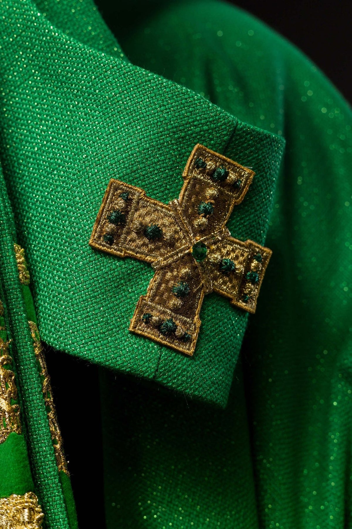 Green chasuble fabric close-up with a gold embroidered cross