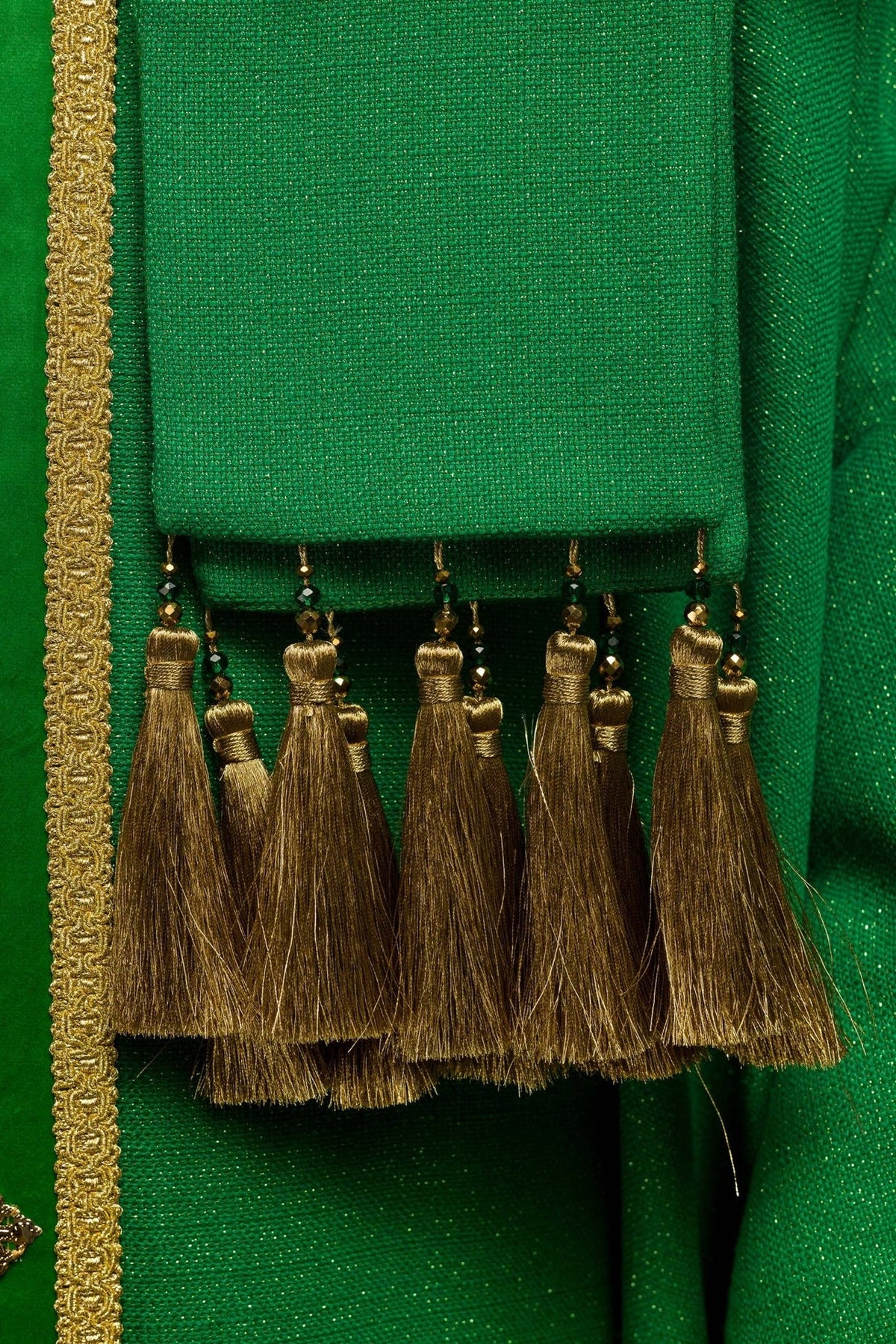 Handcrafted chasuble close-up showing green fabric, gold trim and hanging gold tassels