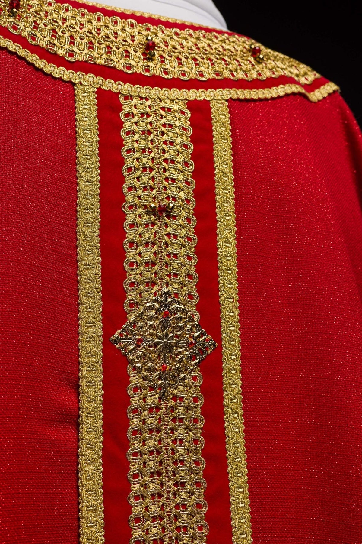 Handcrafted chasuble close-up showing red fabric, gold embroidery and natural stones