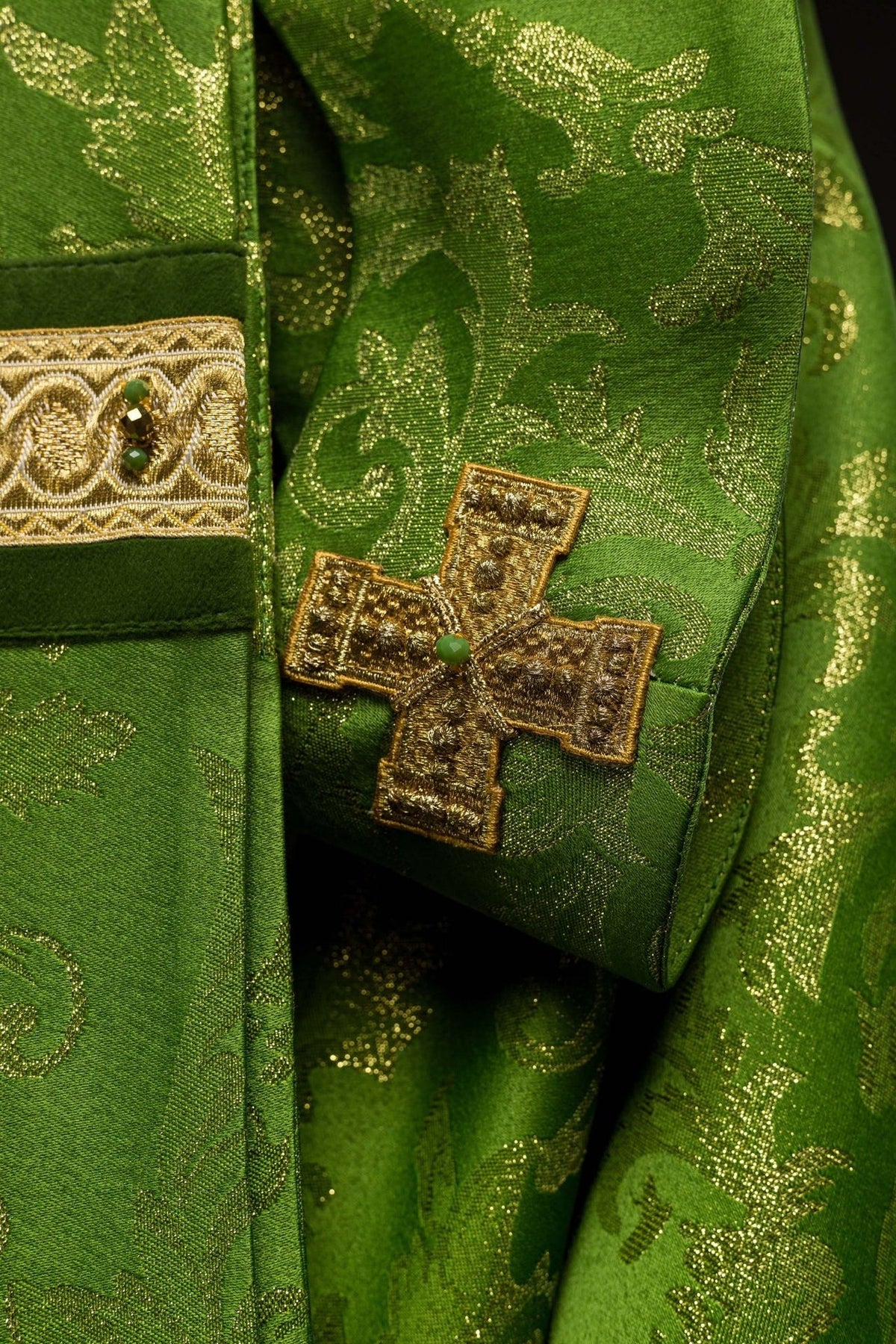 Green chasuble sleeve detail with embroidered gold cross and natural stone
