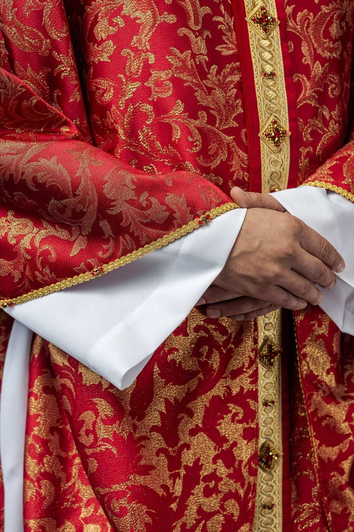 Red chasuble close-up showing gold floral jacquard and jeweled orphrey