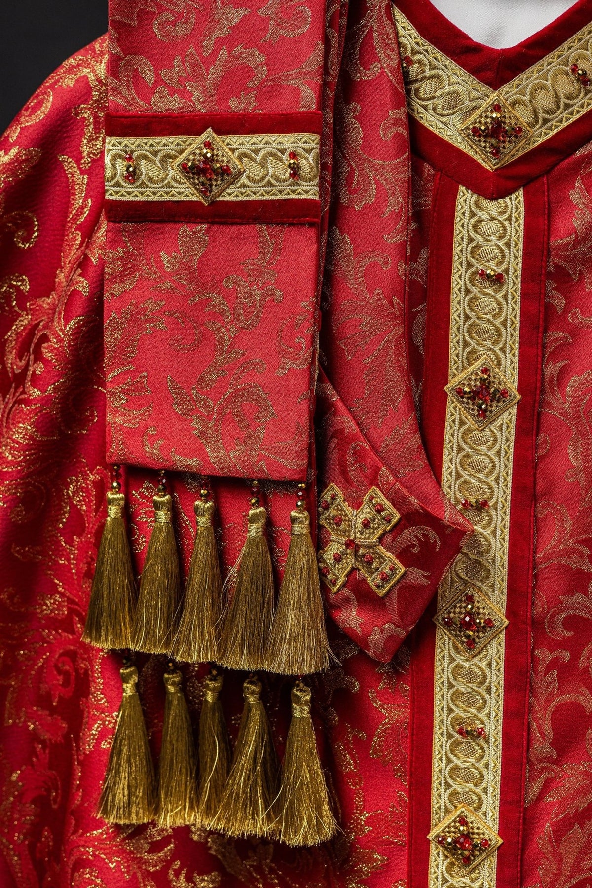 Red chasuble detail with gold tassel trim, jeweled sleeve band and embroidered orphrey