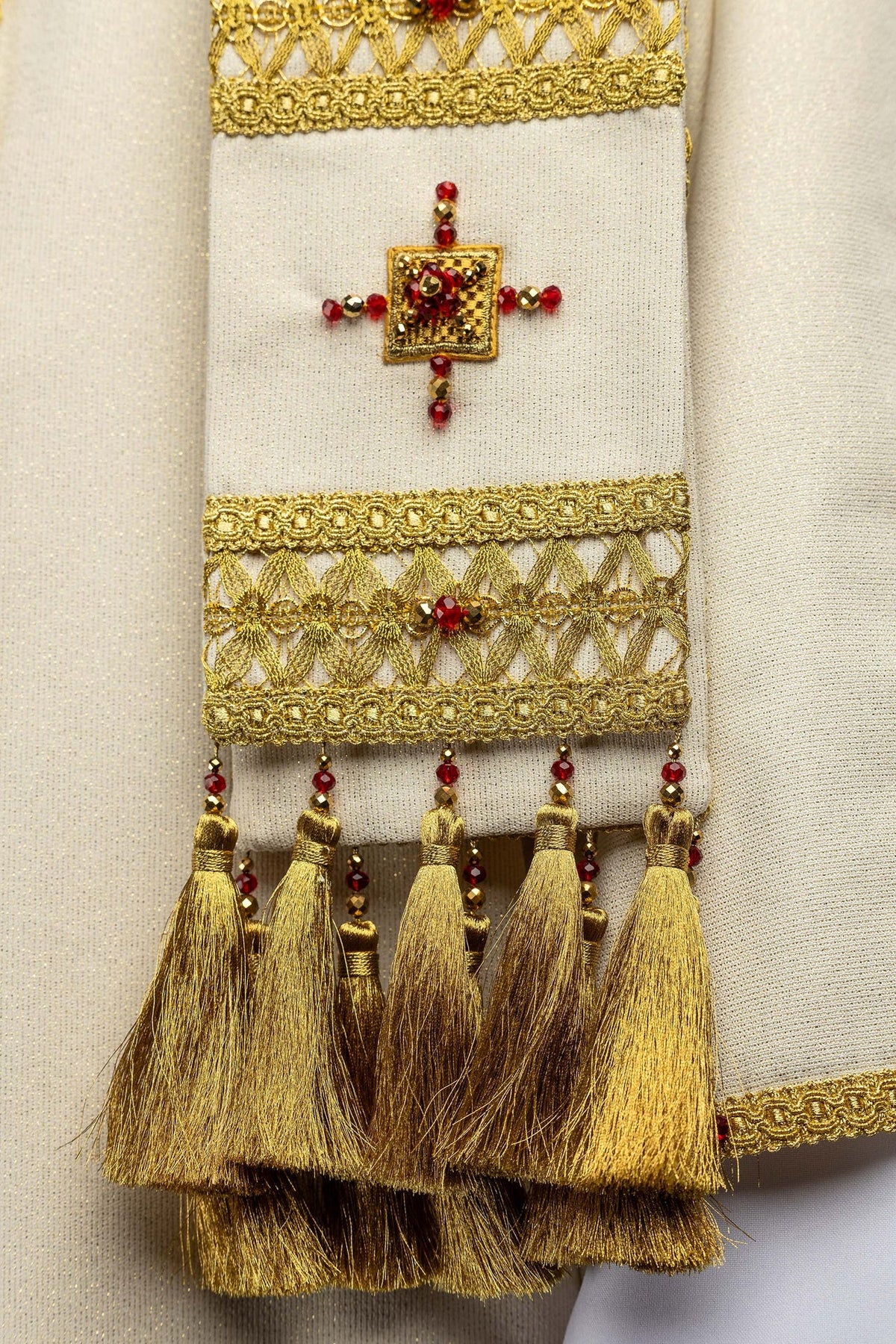 Handcrafted chasuble sleeve close-up with gold openwork, red stones, and hanging gold tassels